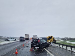 Na prawym pasie jezdni stoi fiat z uszkodzonym tyłem. Obok niego zepchnięty na bariery ochronne znajduje się rozbity volkswagen. Na pasie zieleni rozdzielającym kierunki jazdy stoi natomiast pojazd marki hyundai z uszkodzonym tyłem.