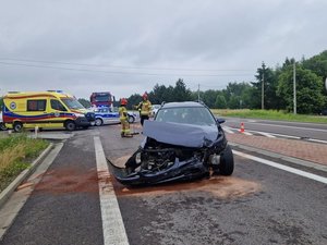 Pojazd marki Mazda stojący na pasie w kierunku Rzeszowa. Samochód ma rozbity przód. Za nim stoi karateka pogotowia, radiowóz i wóz strażacki.