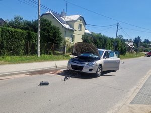 Na jezdni stoi samochód marki hyundai. Pojazd ma rozbitą przednią szybę i urwane lewe lusterko. Pod przednimi kołami samochodu znajduje się rozbita hulajnoga.