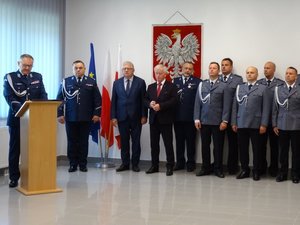 Komendant Powiatowy Policji w Łańcucie stoi przy mównicy i wygłasza okolicznościowe przemówienie. Obok niego stoi Zastępca Komendanta Wojewódzkiego Policji w Rzeszowie, zaproszeni goście oraz kadra kierownicza łańcuckiej komendy.