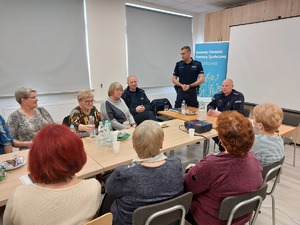 Prelekcje prowadzi asp. Mateusz Szeremeta, który stoi przed siedzącymi przy stołach uczestnikami.