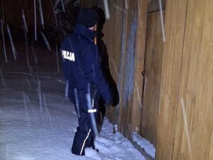Policjant stoi w śniegu przed budynkiem mieszkalnym