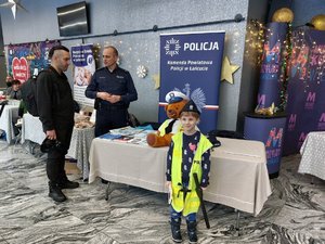 Chłopiec ubrany w kamizelkę z napisem Policja stoi przed policyjnym stoiskiem.