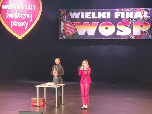 Na scenie MDK kobieta trzyma policyjnego miśka do licytacji.