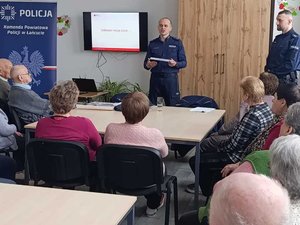 Policjant opowiada o elementach odblaskowych, które trzyma w dłoniach.