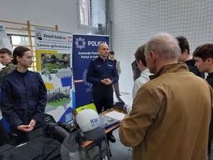 Policjant przy policyjny stoisku prezentuje wyposażenie służbowe.