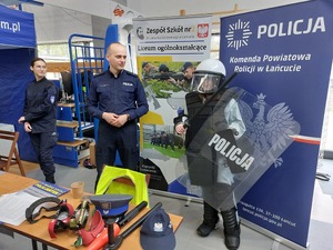 Dziewczyna ubrana w policyjny zestaw przeciwuderzeniowy pozuje do zdjęcia przy policyjnym stoisku.