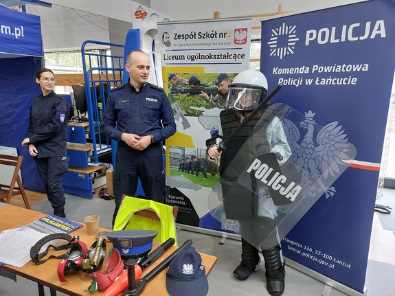 Dziewczyna ubrana w policyjny zestaw przeciwuderzeniowy pozuje do zdjęcia przy policyjnym stoisku.