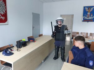 Uczeń ubrany w policyjny zestaw uderzeniowy pozuje do pamiątkowego zdjęcia.