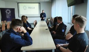 Policjant stoi przed ekranem, na którym wyświetlany jest napis POLICJA.