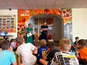 Policjant wraz z przedstawicielką sanepidu rozmawiają z dziećmi na temat bezpiecznych wakacji.